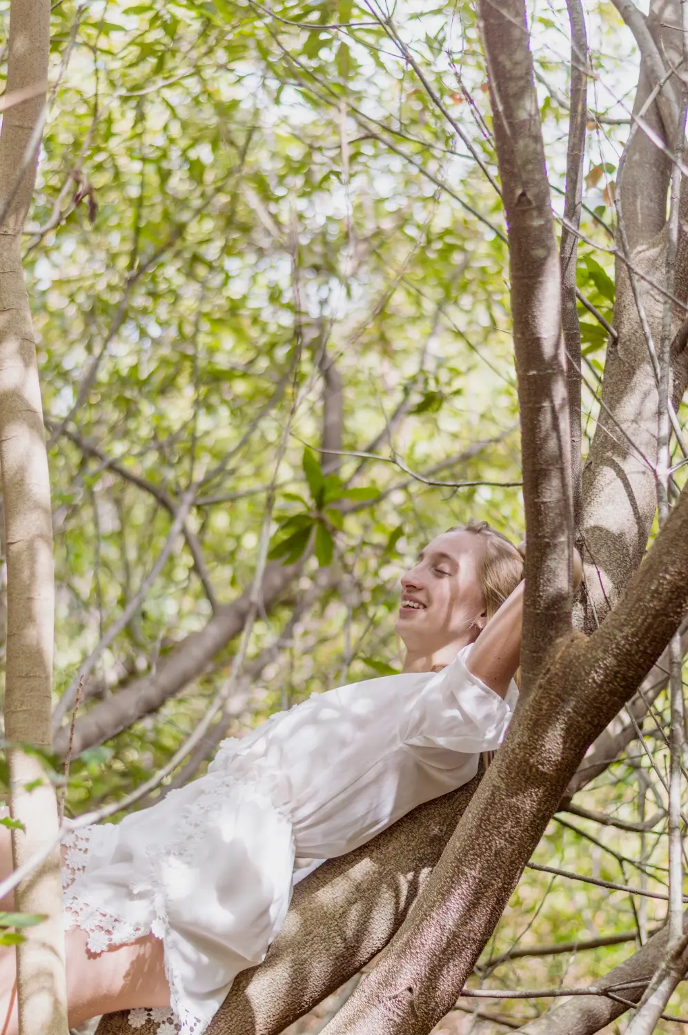Woman smiling and sitting on a sturdy tree branch, representing the strength and resilience built during sessions with a Dr. Phillips therapist.