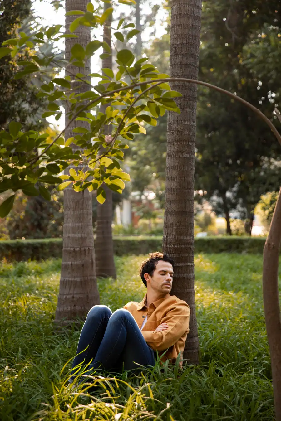 A man sitting against a palm tree with his eyes closed, taking a quiet break from the overstimulation that comes with adult ADHD.